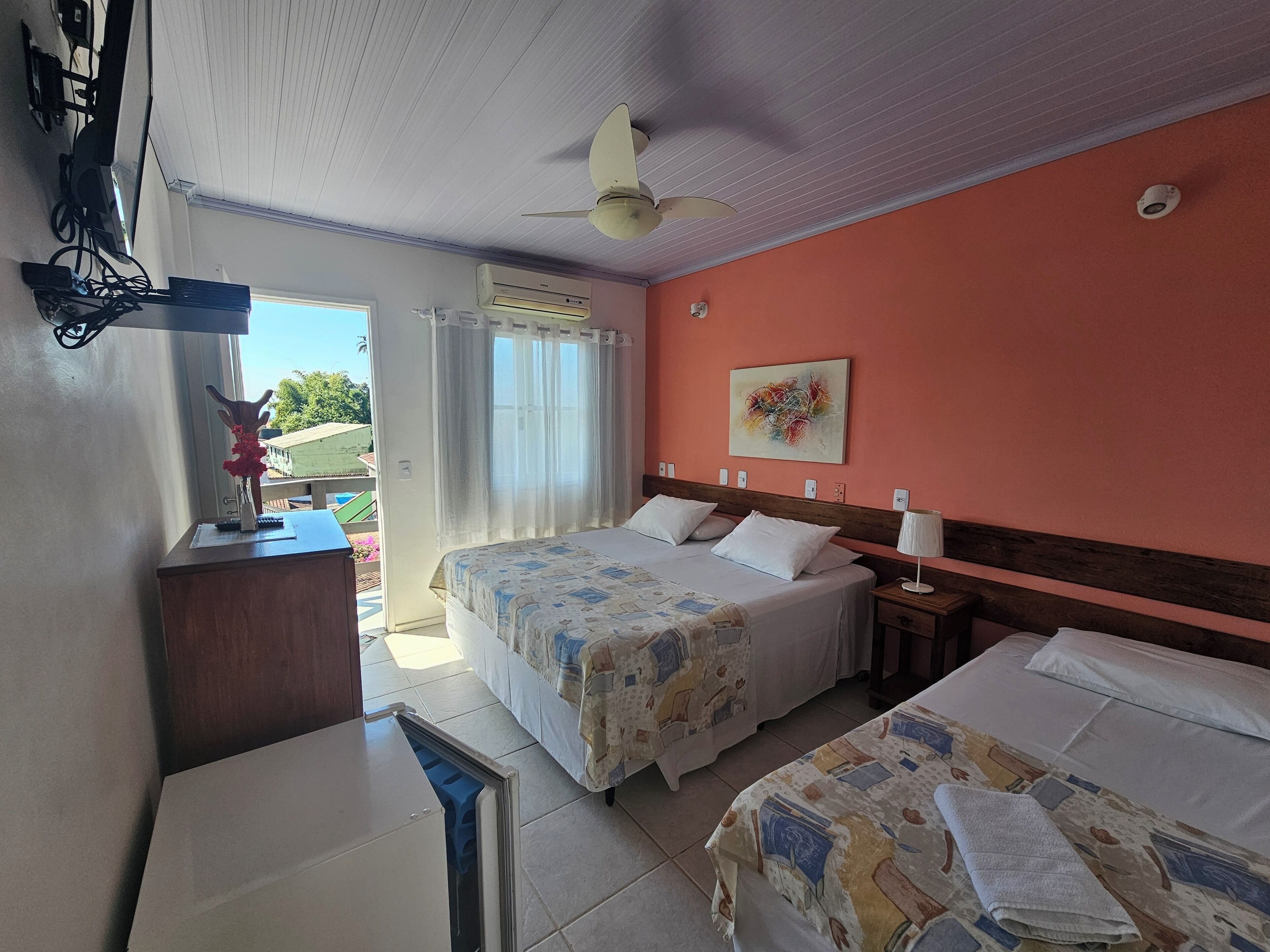 Habitación de hotel con dos camas, ventilador de techo, ventana con cortinas y un cuadro en la pared.