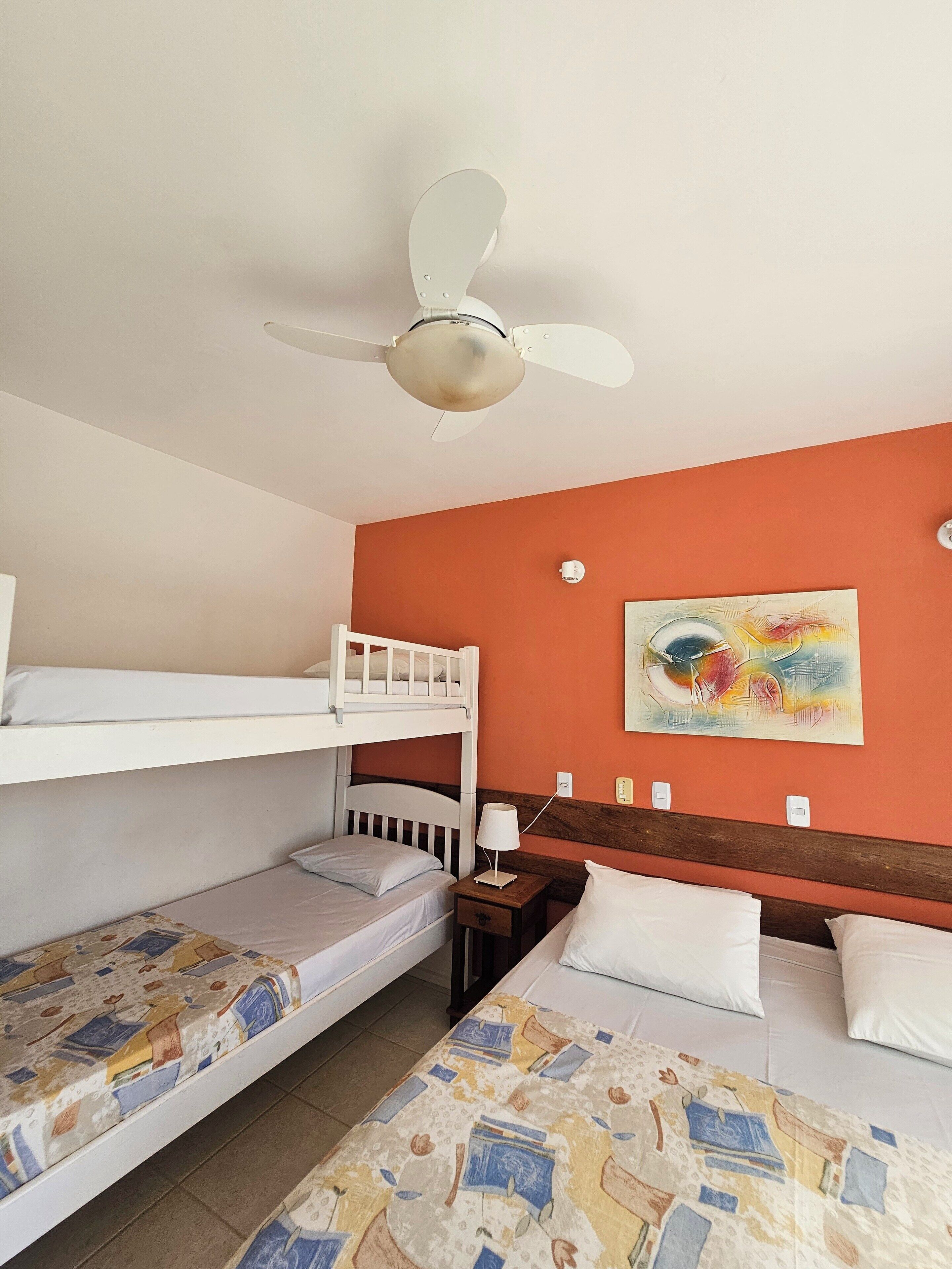 A hotel room with bunk beds, a ceiling fan, a painting on the wall, and a bedside table with a lamp.