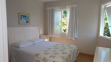 A bedroom with a bed, a nightstand, a window with curtains, and a framed picture on the wall.