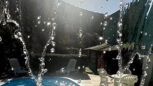 A swimming pool with water jets spraying upwards, surrounded by outdoor furniture and a mountainous backdrop. - Pousada Anambé (Angra dos Reis)