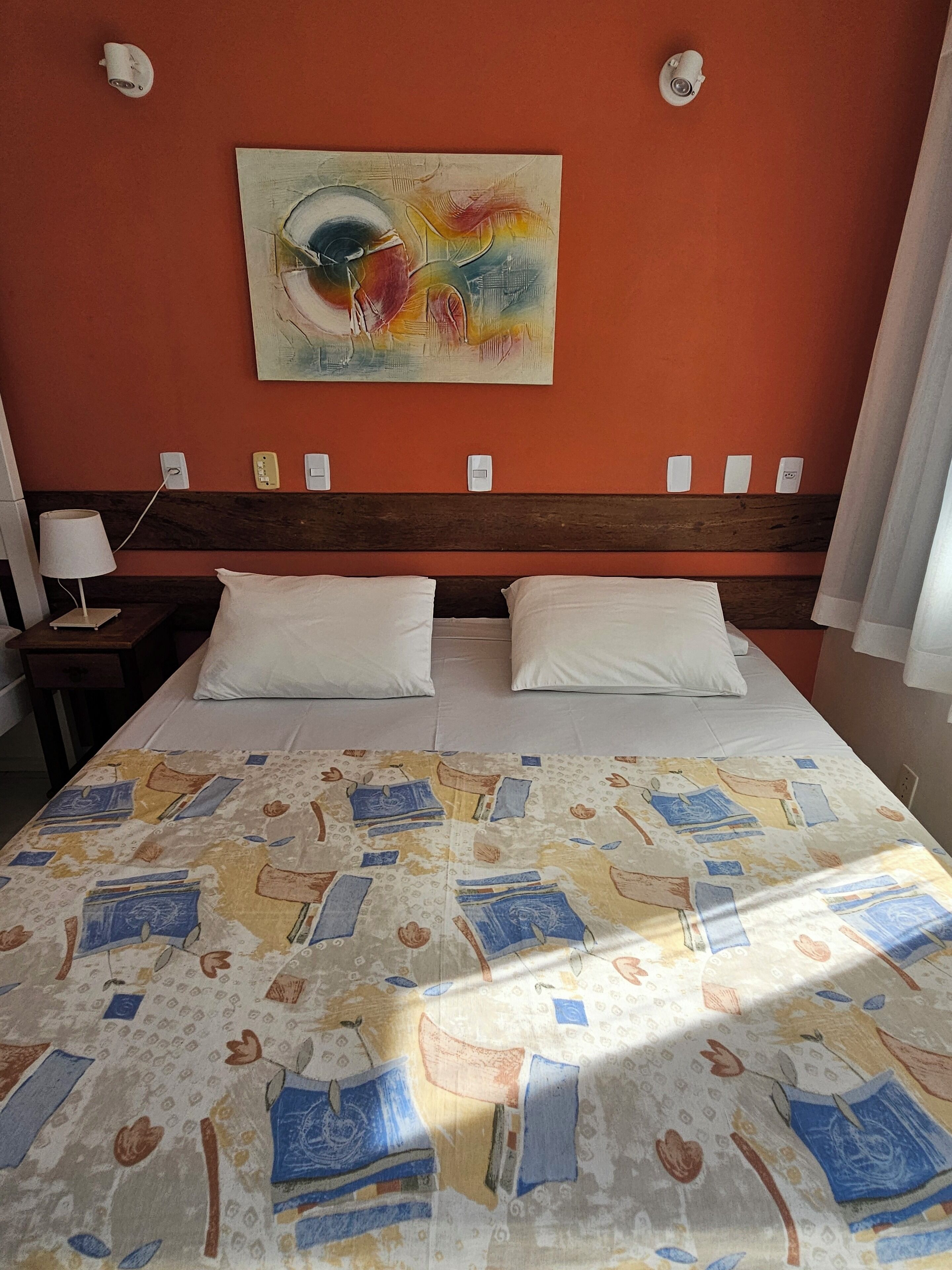 Una habitación de hotel con una cama, una mesita de noche, una lámpara y un cuadro en la pared.