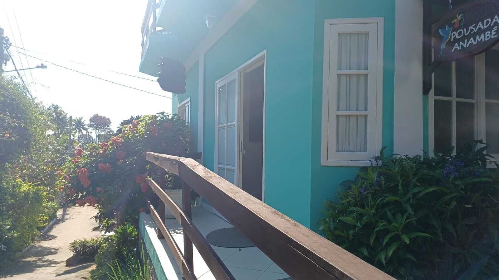 Un edificio turquesa con barandal de madera, una puerta y una ventana.