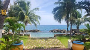 A paved pathway leading to a beach with palm trees and a sign warning of falling coconuts. - Charming 1-bedroom in Tower Isle St Mary: AC, WiFi, pool, and a serene retreat. (Tower Isle)