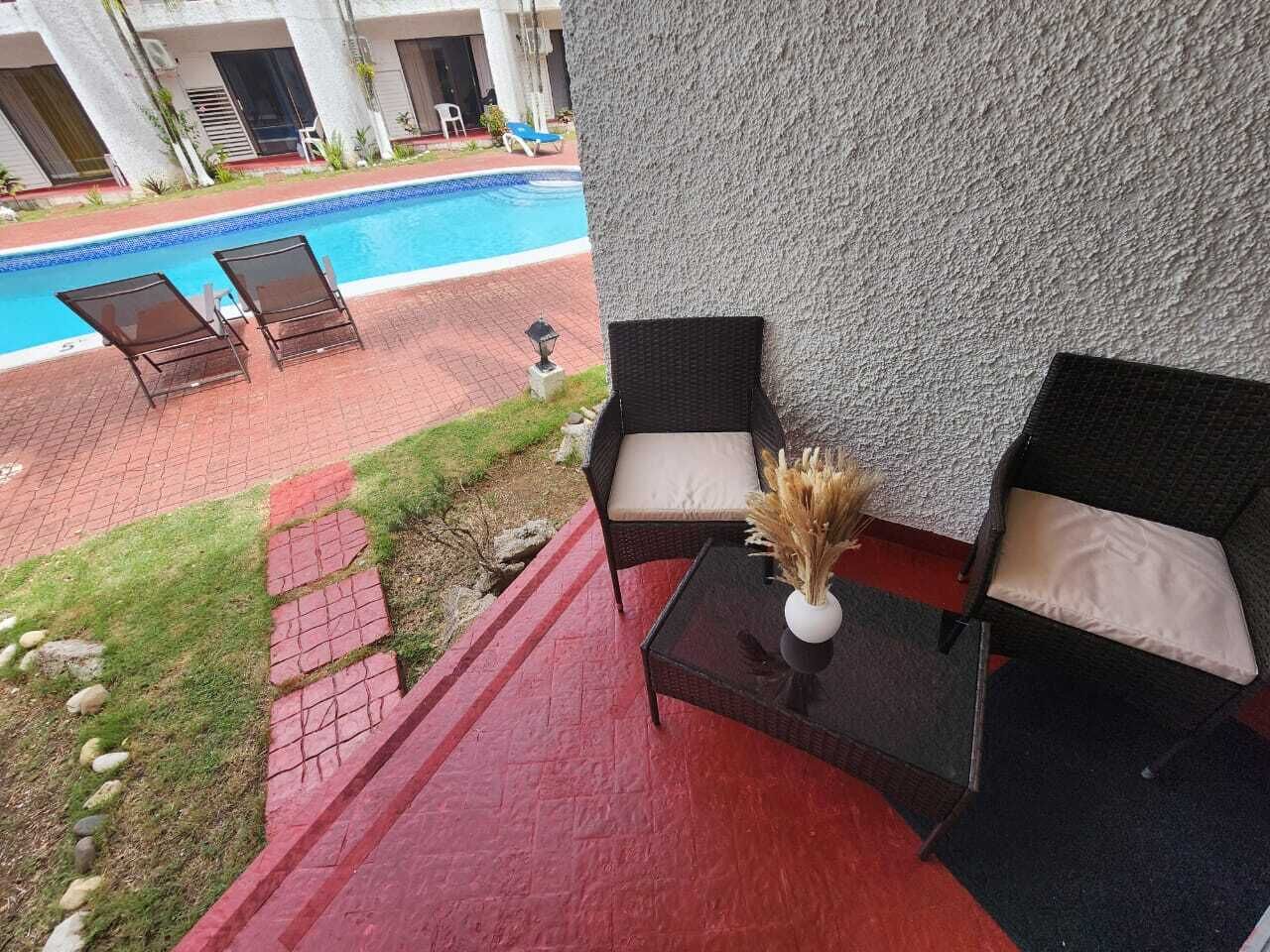A poolside area with two wicker chairs, a glass table, and a vase of dried flowers.