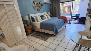 A bedroom with a bed, a desk, chairs, a small rug, and a view of the outside. - Charming 1-bedroom in Tower Isle St Mary: AC, WiFi, pool, and a serene retreat. (Tower Isle)