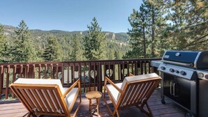 A deck with two wooden chairs and a small table, overlooking a forested area with mountains in the background. - Renovated Ski Home with a Hot Tub & Views of Slope - Perfect Ski Lease (Incline Village)