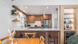 A modern kitchen with wooden cabinets, a central island, and a dining area with chairs. - Renovated Ski Home with a Hot Tub & Views of Slope - Perfect Ski Lease (Incline Village)
