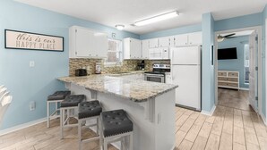 A modern kitchen with white cabinets, a granite island with bar stools, a microwave, oven, and a built-in brick backsplash. - 2 Bikes~ Newly renovated Pool~Bike to Seaside (Santa Rosa Beach)