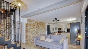 A living room with a stone wall, a grey sofa, a staircase with metal railings, and a kitchen in the background.