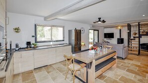 A modern kitchen with a central island, a dining area with a wooden table and chairs, a built-in oven, and a TV mounted on the wall.