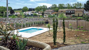 A backyard with a swimming pool, stone wall, and various plants.