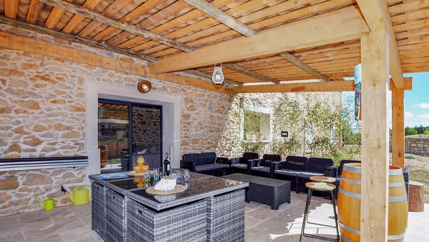 An outdoor patio with stone walls, a wooden ceiling, and a seating area with sofas and tables.