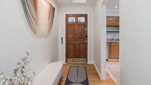 Un couloir avec une porte en bois, un banc et un tapis menant à un espace cuisine.