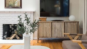 Un salon avec une cheminée, un téléviseur fixé au-dessus, un meuble en bois et un canapé gris.