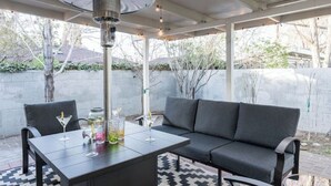 Une terrasse extérieure avec une table noire, deux chaises et un canapé gris.