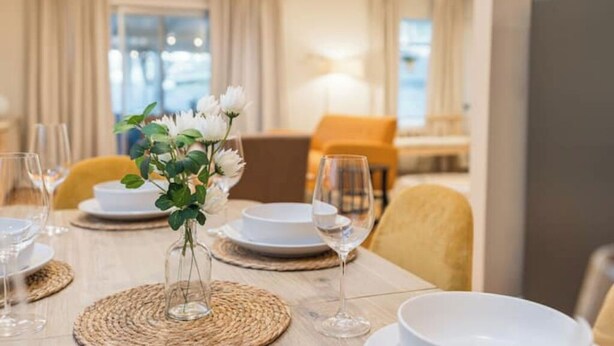 Une table à manger dressée avec de l’assiette blanche, des verres à vin et un vase contenant des fleurs blanches.
