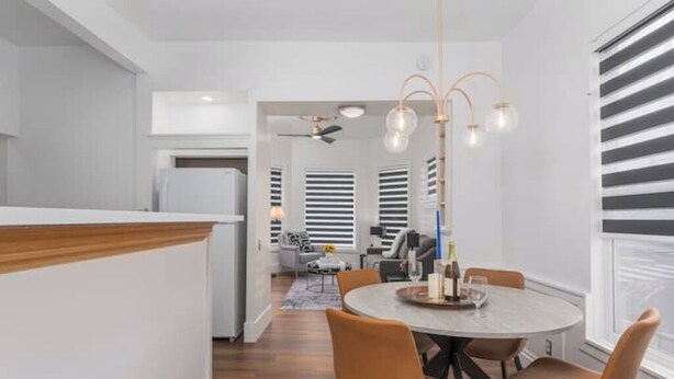 Een moderne keuken met een houten aanrecht, een eethoek met een ronde tafel en oranje stoelen, en een plafondventilator.
