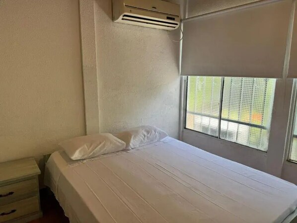 A single bed with white bedding, a window with a view of greenery, and an air conditioning unit on the wall. - Superior Family Room (Villavicencio)