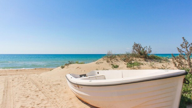 Ein Boot an einem sandigen Strand, bewölkter Himmel und ruhiges Meer.