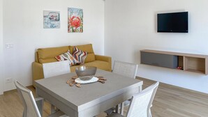 Ein modernes Wohnzimmer mit einer Couch, einem Esstisch mit Stühlen, einem an der Wand montierten Fernseher und Wandbildern.