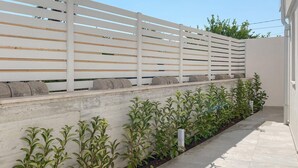 Eine moderne Außenpatio mit weißem Lattenzaun, einer Betonmauer und Grünpflanzen.