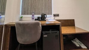 A compact workspace with a desk, chair, and a small black refrigerator. - Wishotel Premier Parth Residency (Deoria)