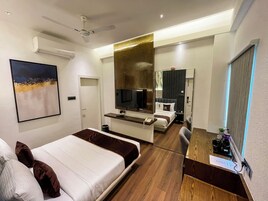 Habitación de hotel moderna con cama, escritorio, televisor y baño visible a través de una puerta abierta.