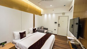 A hotel room with a bed, a desk with a telephone, a television, and a ceiling fan. - Wishotel Premier Parth Residency (Deoria)