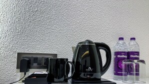A coffee maker, two Bailey water bottles, and two glasses on a table. - Wishotel Premier Parth Residency (Deoria)