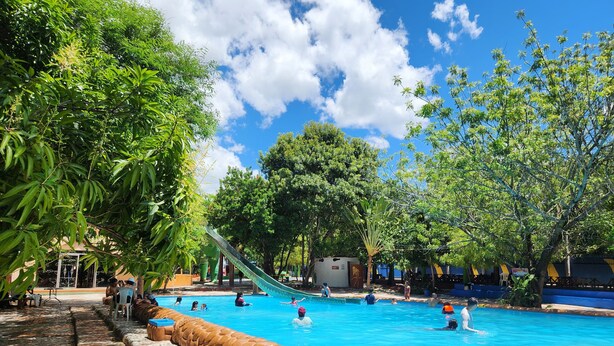 A swimming pool with a slide, surrounded by trees and a tiled walkway.