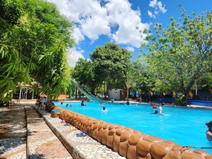 A swimming pool with a slide, surrounded by trees and a tiled walkway.