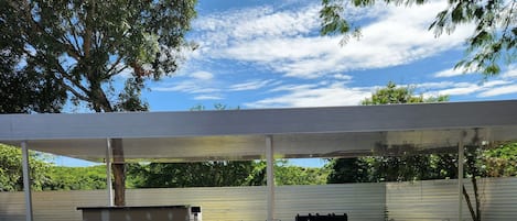 Una piscina con un porche cubierto, una parrilla y mobiliario de exterior.