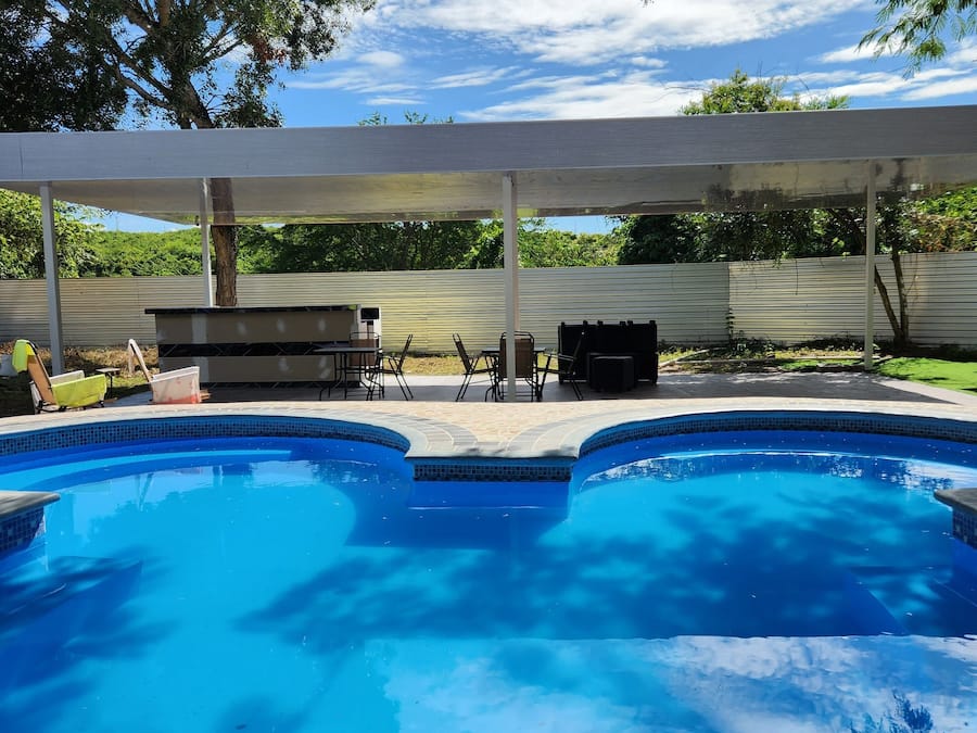 A swimming pool with a covered patio area, a barbecue grill, and outdoor seating.