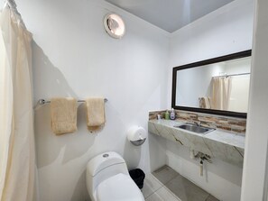 A bathroom with a toilet, two towels, a sink with a marble countertop, a mirror, and a shower curtain.