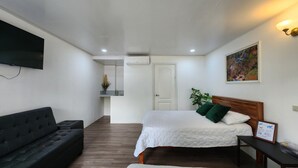 A bedroom with a bed, a sofa, a TV, a painting, and a door leading to a bathroom.