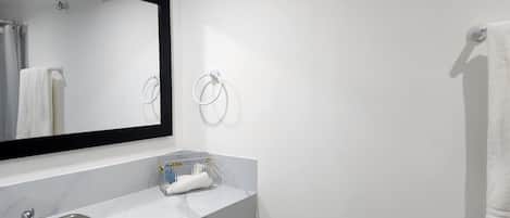 Un baño con un lavamanos blanco, un espejo y dos anillos para toallas en la pared.