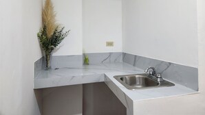 A kitchen with a marble countertop, a stainless steel sink, and a vase with dried plants.