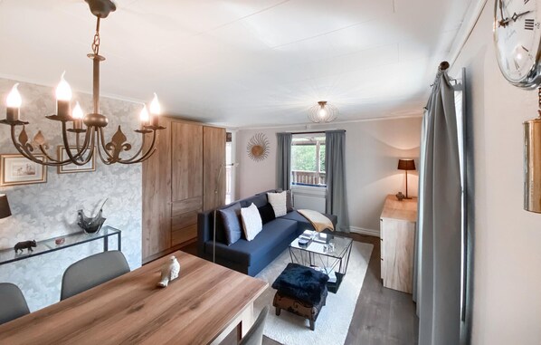 A cozy living room with a sofa, a wooden dining table, and a chandelier.