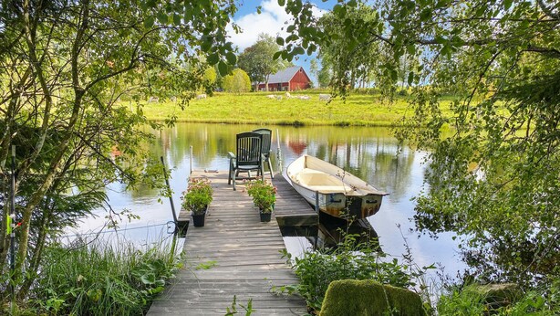 A wooden dock leading to a calm lake, with a boat tied to the dock and a chair and potted plants nearby. - Nice home in Sävsjö with WiFi (Sävsjö)