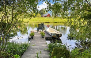 A wooden dock leading to a calm lake, with a boat tied to the dock and a chair and potted plants nearby.