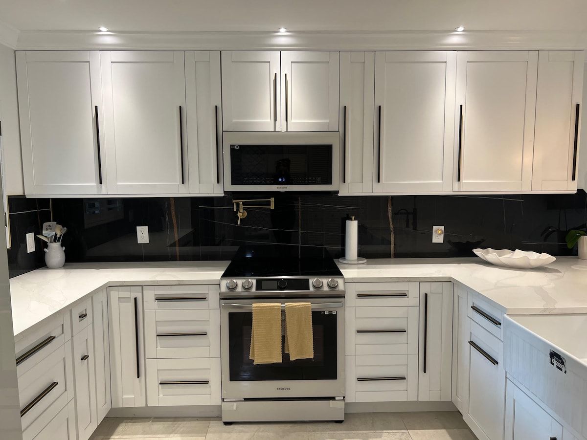 Una cocina moderna con armarios blancos, encimera negra y electrodomésticos de acero inoxidable.
