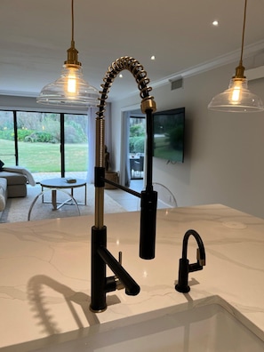 Una cocina moderna con encimera de mármol blanco, grifo negro y dos lámparas colgantes con pantallas de cristal.