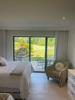 Un dormitorio con cama, una silla, un aparador y vistas a un jardín a través de un ventanal.
