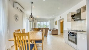 Eine moderne Küche mit Essbereich, ausgestattet mit einem Holztisch, Stühlen, einer Pendelleuchte und Blick ins Freie durch große Fenster.