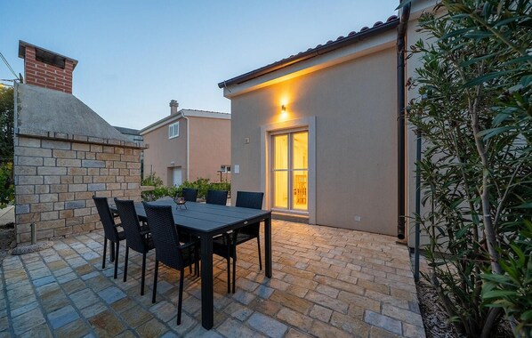 A patio with a table and chairs, a brick wall, and a building with a lit window.