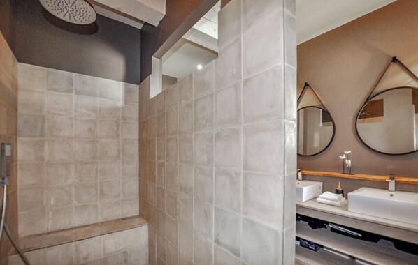 Un baño moderno con ducha, dos espejos montados en la pared y un tocador con lavabo y dispensador de toallas.