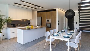 Una cocina moderna con una isla central, electrodomésticos integrados y un comedor con sillas blancas y platos azules.