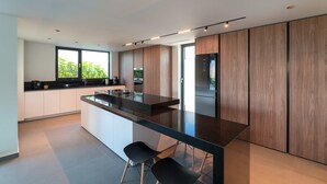 Een moderne keuken met een centraal eiland, witte kasten en een groot raam dat voor natuurlijk licht zorgt.