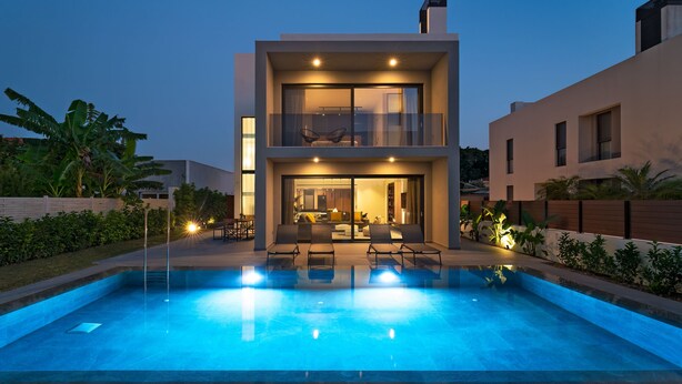 Een modern huis met twee verdiepingen, een zwembad, terras en een goed verlicht interieur.