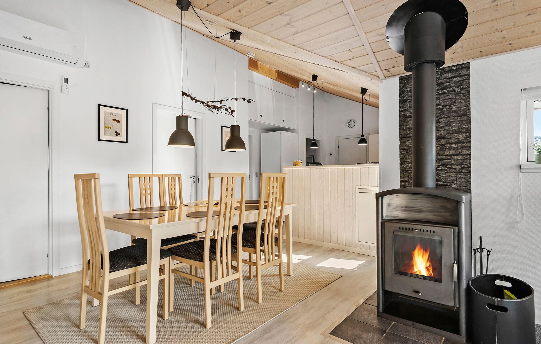 A modern kitchen with a central island, wooden chairs, a dining table, and a wood-burning stove.